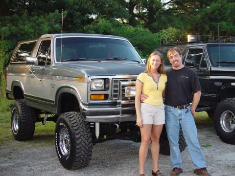 1989 Ford Bronco - A couple stands in front of a lifted 1980s Ford Bronco, with another truck visible behind them.