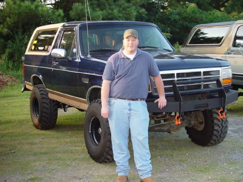 1989 Ford Bronco - A man poses in front of a lifted blue 1989 Ford Bronco with a tan removable top and a custom front bumper.
