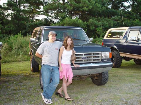 1989 Ford Bronco - Couple poses with a dark blue Ford Bronco; another similar vehicle is parked nearby.