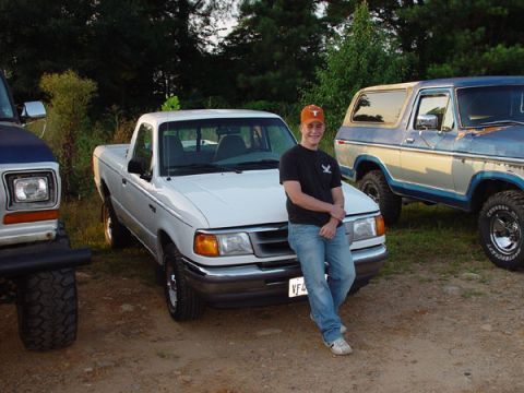 1989 Ford Bronco - A white Ford Ranger pickup truck is parked next to a blue Ford Bronco, with a young man leaning against the truck.