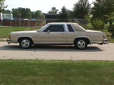 1985 Ford LTD Crown Victoria - Driver-side profile of a cream/tan two-door Ford Crown Victoria coupe with an opera-style rear quarter window and formal roofline, parked o…