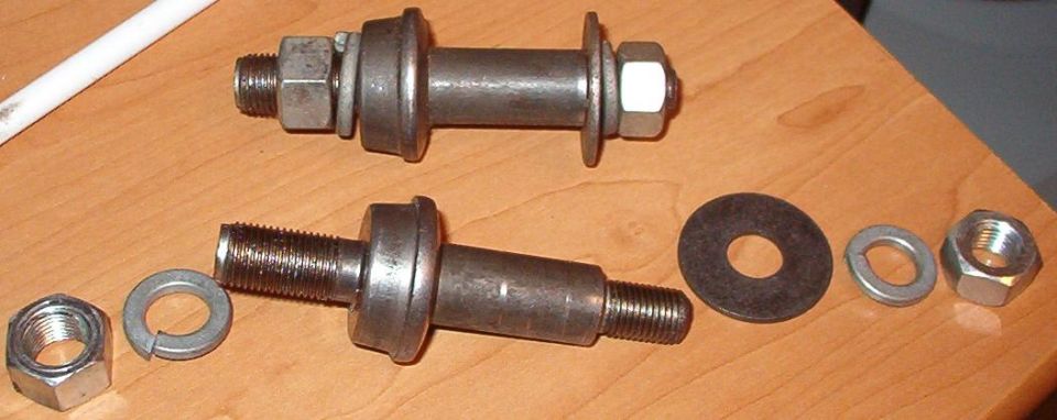 Two threaded suspension bolts or pins with nuts and washers laid on a wooden table