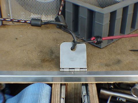 1993 Ford Bronco - Close-up of a small bare aluminum bracket or flap with a drilled hole, hinged to a length of aluminum angle stock on a workbench. Black and…