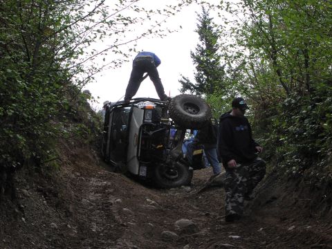 1993 Ford Bronco - An off-road vehicle is stuck on a steep, wooded trail with several people attempting to help.