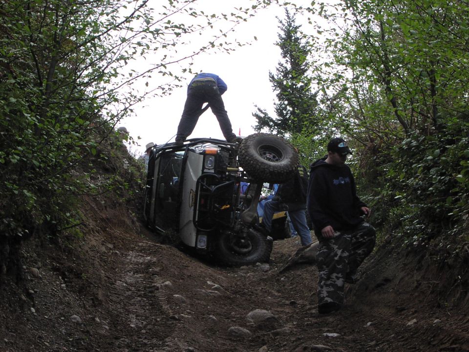Off-road vehicle tipped on its side on a dirt trail with people around it
