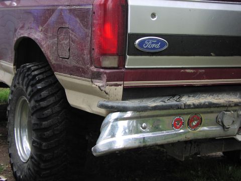 1993 Ford Bronco - Rear view of a maroon and tan Ford Bronco with off-road tires and a chrome bumper, showing signs of wear and tear.