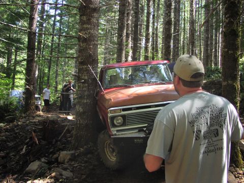 1993 Ford Bronco - Off-road vehicle navigating a tight spot between trees on a wooded trail.