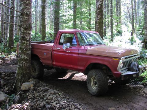 1993 Ford Bronco - A red pickup truck with a brown hood navigates a wooded trail.