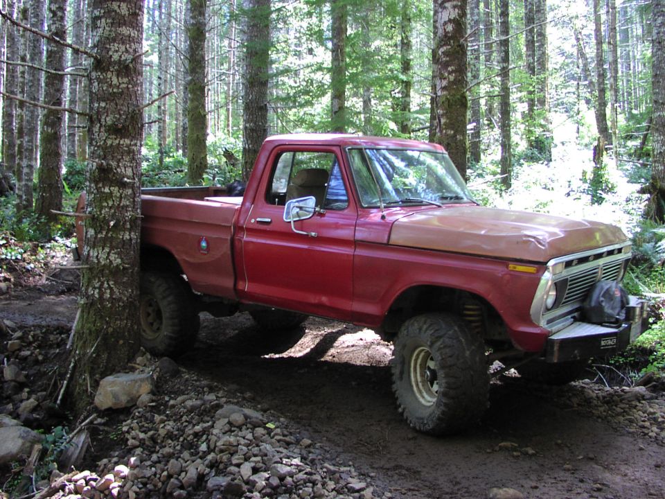 Red pickup truck with a brown hood, off-roading in a forest