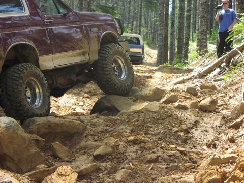 1993 Ford Bronco - Two Ford Broncos navigate a challenging rocky off-road trail through a forest.