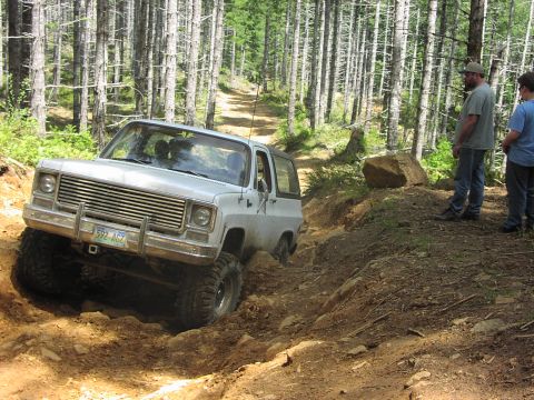 1993 Ford Bronco - This lifted SUV is tackling a challenging off-road trail with steep inclines and rocky terrain.