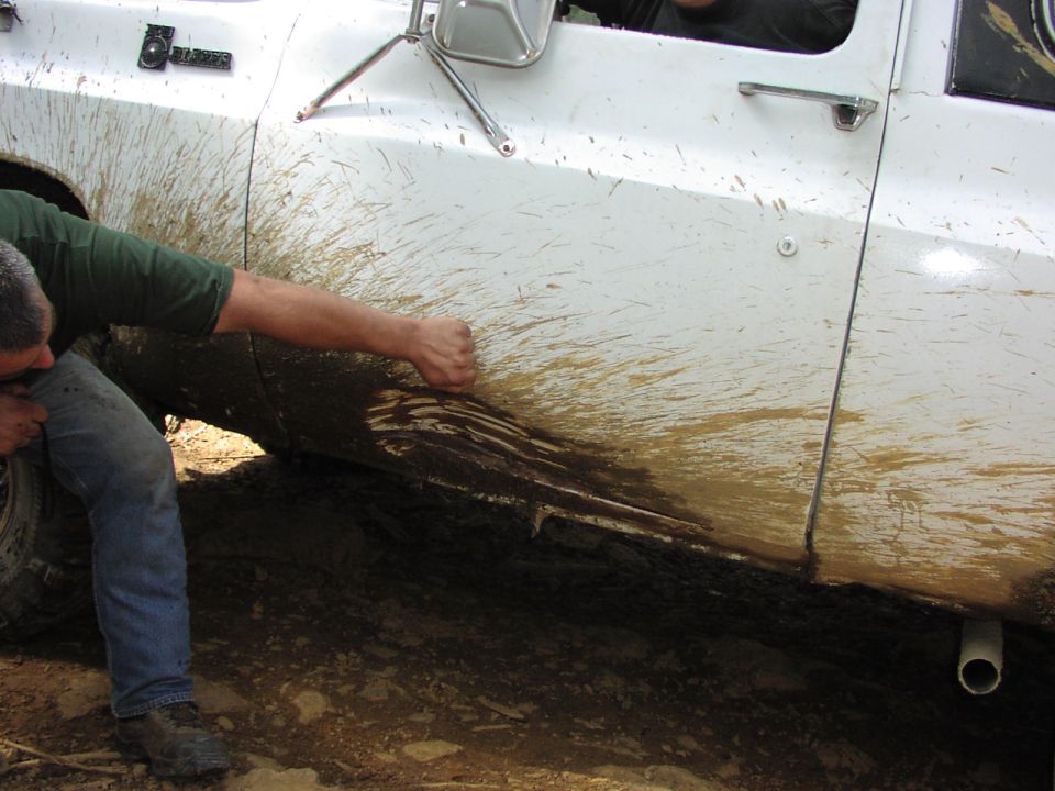 White SUV door with mud splatters, a person in jeans and a green shirt is cleaning it