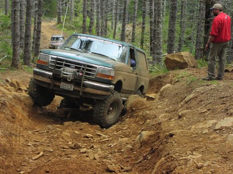 1993 Ford Bronco - A green Ford Bronco navigates a challenging off-road course with another vehicle in the background.