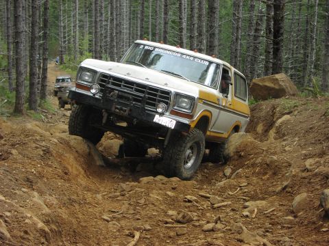 1993 Ford Bronco - Two Ford Broncos navigate a challenging off-road trail through a forest.