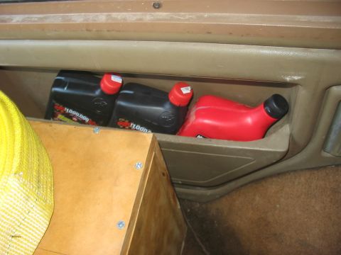 1988 Ford Bronco - A storage cubby holds various fluid containers and a yellow strap.