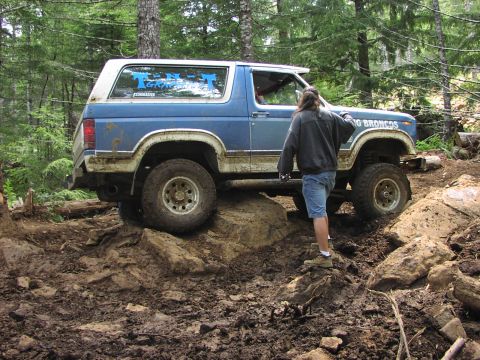 1993 Ford Bronco - This blue and white SUV is shown off-roading on a muddy and rocky trail. Text on the door indicates it is a 'BIG BRONCOS'.