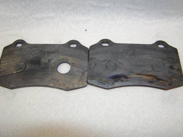 Two worn brake pad backing plates with heat marks on a white paper towel