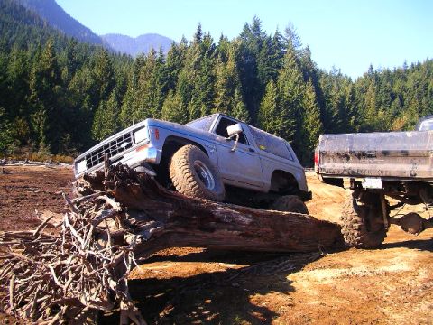 1984 Ford Bronco II - An SUV navigates a challenging off-road obstacle course in a wooded area.