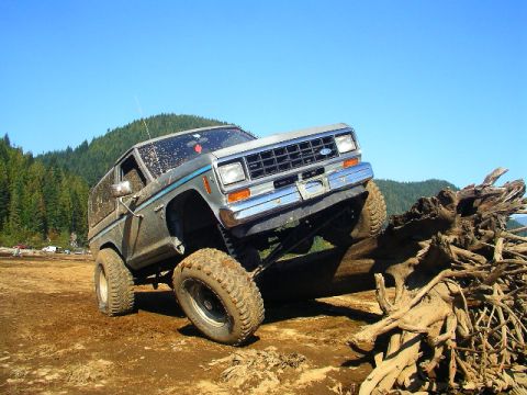 1984 Ford Bronco II - A lifted 1983 Ford Bronco II navigates a challenging off-road course, climbing over a massive tree root.