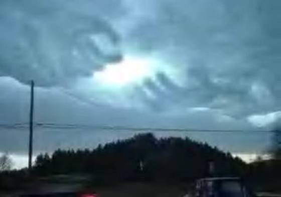 stormy sky with bright sun breaking through clouds over a dark treeline and a utility pole