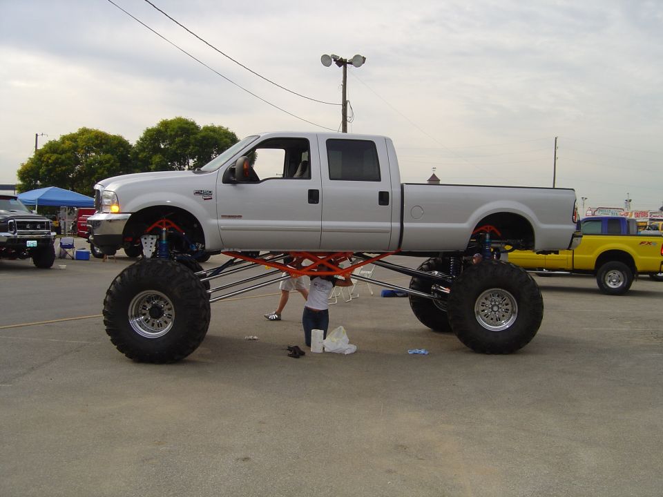 Silver lifted pickup truck with oversized tires and orange suspension components, viewed from the side