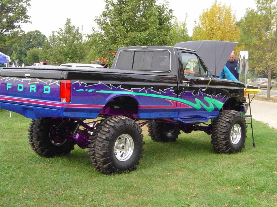Lifted black Ford truck with purple and teal graphics, side view
