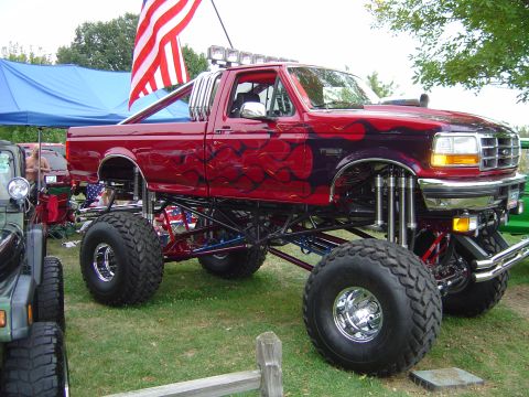 1978 Ford Bronco - A heavily modified red pickup truck with custom flame paint and an extreme lift kit is displayed outdoors.