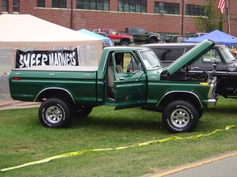1978 Ford Bronco - A green pickup truck is displayed with its hood and driver's door open, under a tent at an outdoor event.