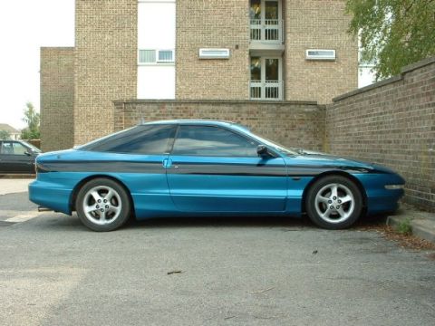 1994 Ford Probe - A side profile of a blue 1994 Ford Probe with a black stripe is parked in front of a brick building.