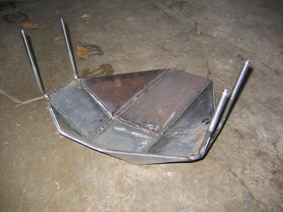 Custom metal skid plate with four metal rods sticking out, resting on a concrete surface