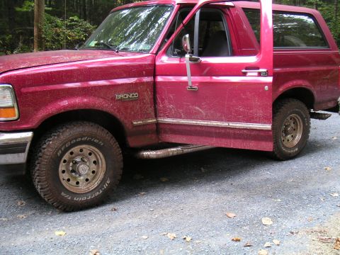 1994 Ford Bronco - A red 1994 Ford Bronco is shown with both driver's side doors ajar, parked on a gravel surface.