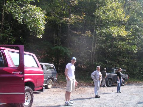 1994 Ford Bronco - Two Ford Bronco SUVs are parked on a dirt road in a wooded area with several people standing around.