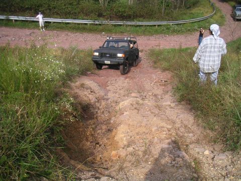 1994 Ford Bronco - A dark gray Ford Bronco drives on a challenging dirt trail with people watching.