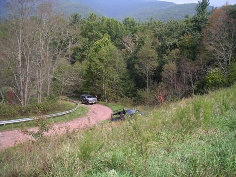 1994 Ford Bronco - Two SUVs navigate a dirt road on a wooded hillside with mountains in the background.