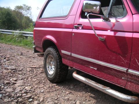 1994 Ford Bronco - Red Ford Bronco on a gravel road, showing its side profile and off-road tires.