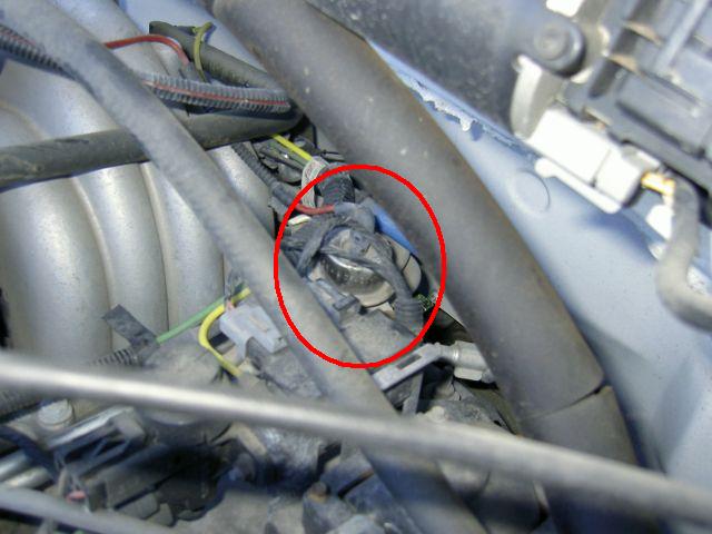 Engine bay close-up with red circle highlighting a part among wiring and intake components