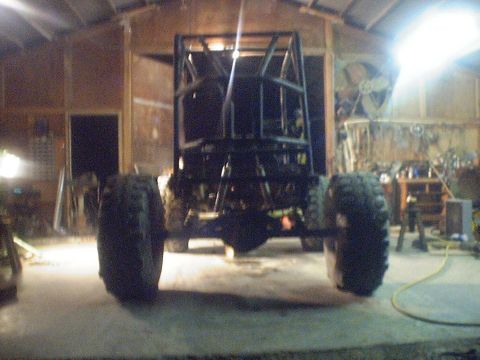 1989 Ford Bronco - The rear view of a custom-built buggy frame with a roll cage and large off-road tires inside a workshop.