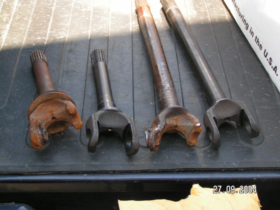 Four driveshaft yokes and shafts, two rusty and two clean, laid out on a dark surface