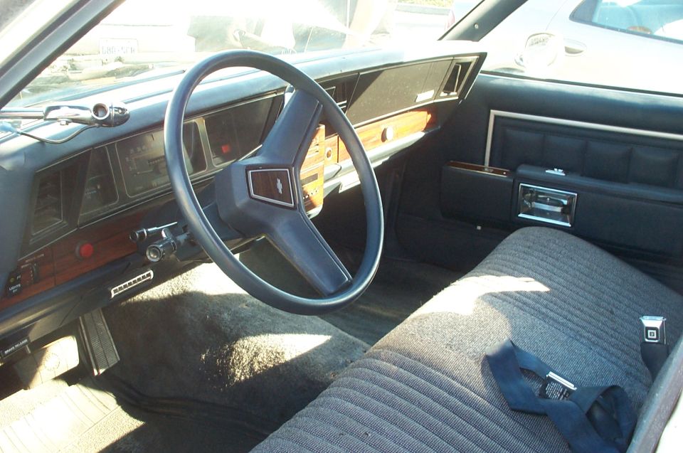 Car interior with blue steering wheel, wood-grain trim, and striped fabric seats. A "SUPERMOTORS" watermark is visible