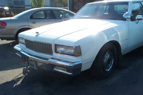 1995 Ford Crown Victoria - A white Chevrolet Caprice is parked next to another vehicle, showing its front grille and headlights.