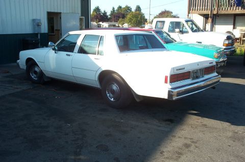 1995 Ford Crown Victoria - A white sedan is parked outside a building, with other vehicles visible in the background.
