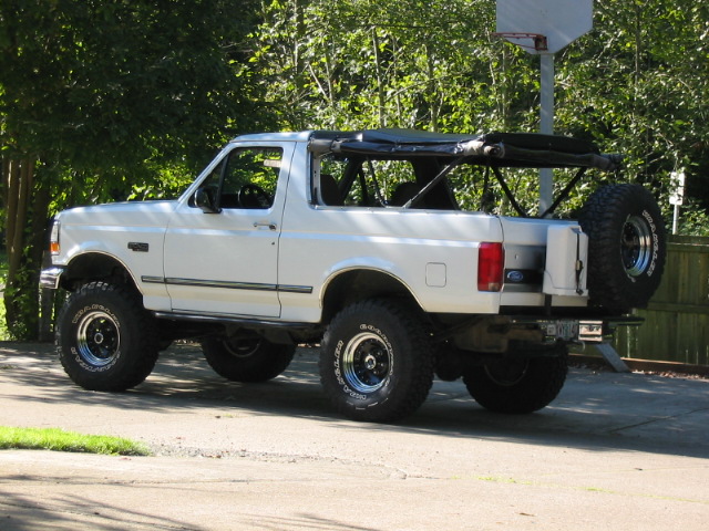 White Ford Bronco with top off, lift kit and off-road tires, rear 3/4 view