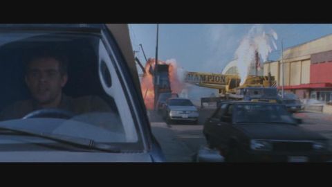1998 Ford Taurus - A man drives a car while a large explosion erupts behind him, with a crane visible in the background.
