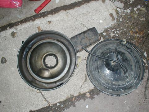 1979 Ford Bronco II - An air cleaner assembly, likely from an older vehicle, is shown disassembled on a concrete surface.