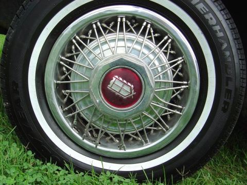 1985 Mercury Grand Marquis - A close-up view of a wire wheel hubcap with a red emblem and whitewall tire.