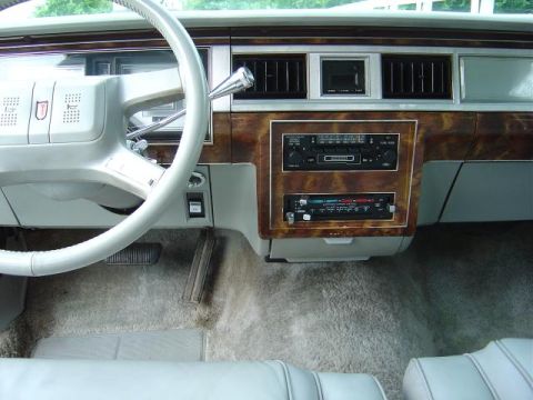 1985 Mercury Grand Marquis - The interior of a 1985 Mercury Grand Marquis features a wood-grain dashboard, a white steering wheel, and an AM/FM cassette stereo.