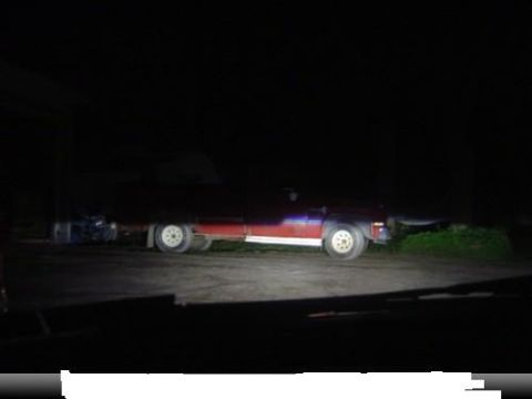 1998 Ford Taurus - A red and blue flatbed truck is parked with a trailer attached, illuminated by headlights in the dark.