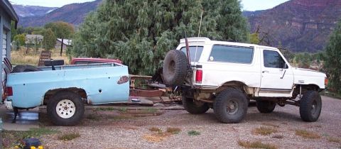 1990 Ford Bronco - White 1990 Ford Bronco tows a light blue pickup truck bed on a trailer.