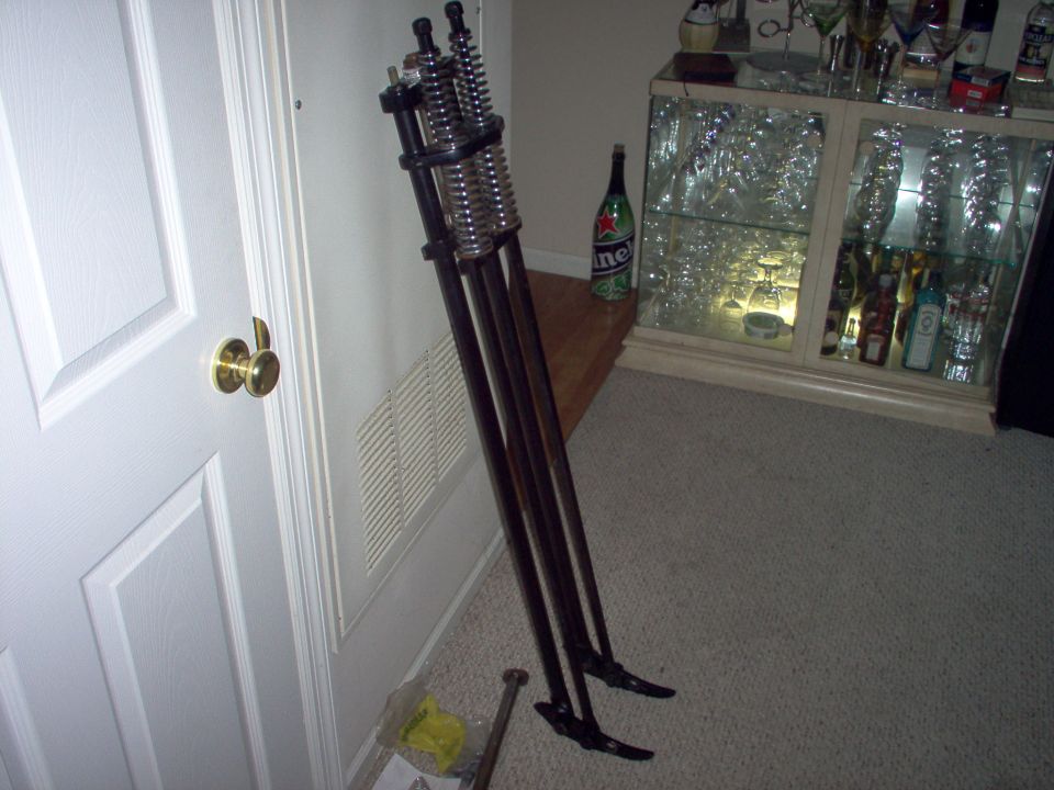 Motorcycle front suspension forks with dual springs, leaning against a wall next to a white door