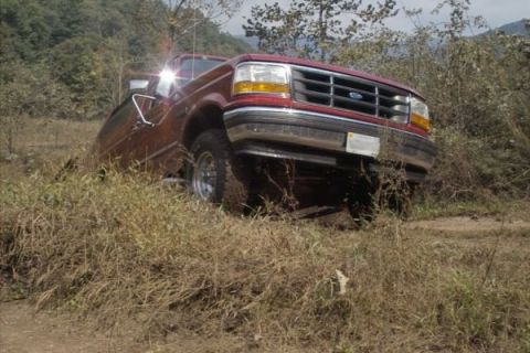 1994 Ford Bronco - A red Ford truck is partially submerged in dry grass and brush, seen from the front-right.